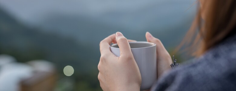 Frau mit Tasse sitz im Grünen und guckt auf die Berge