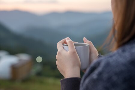 Frau mit Tasse sitz im Grünen und guckt auf die Berge