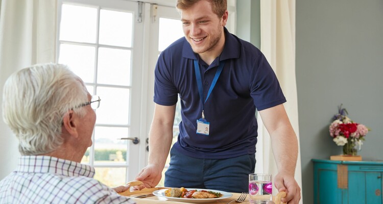 junger Altenpfleger bringt Bewohner Tablett mit Essen