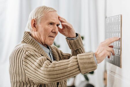 älterer Mann vor Kalenderblatt stehend mit Hand an Stirn schaut dieses verunsichert an