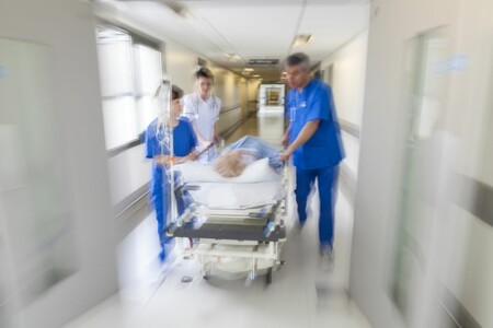 Team aus Ärzten und Pflegern mit Patient auf Liege durch Krankenhausflur rasend